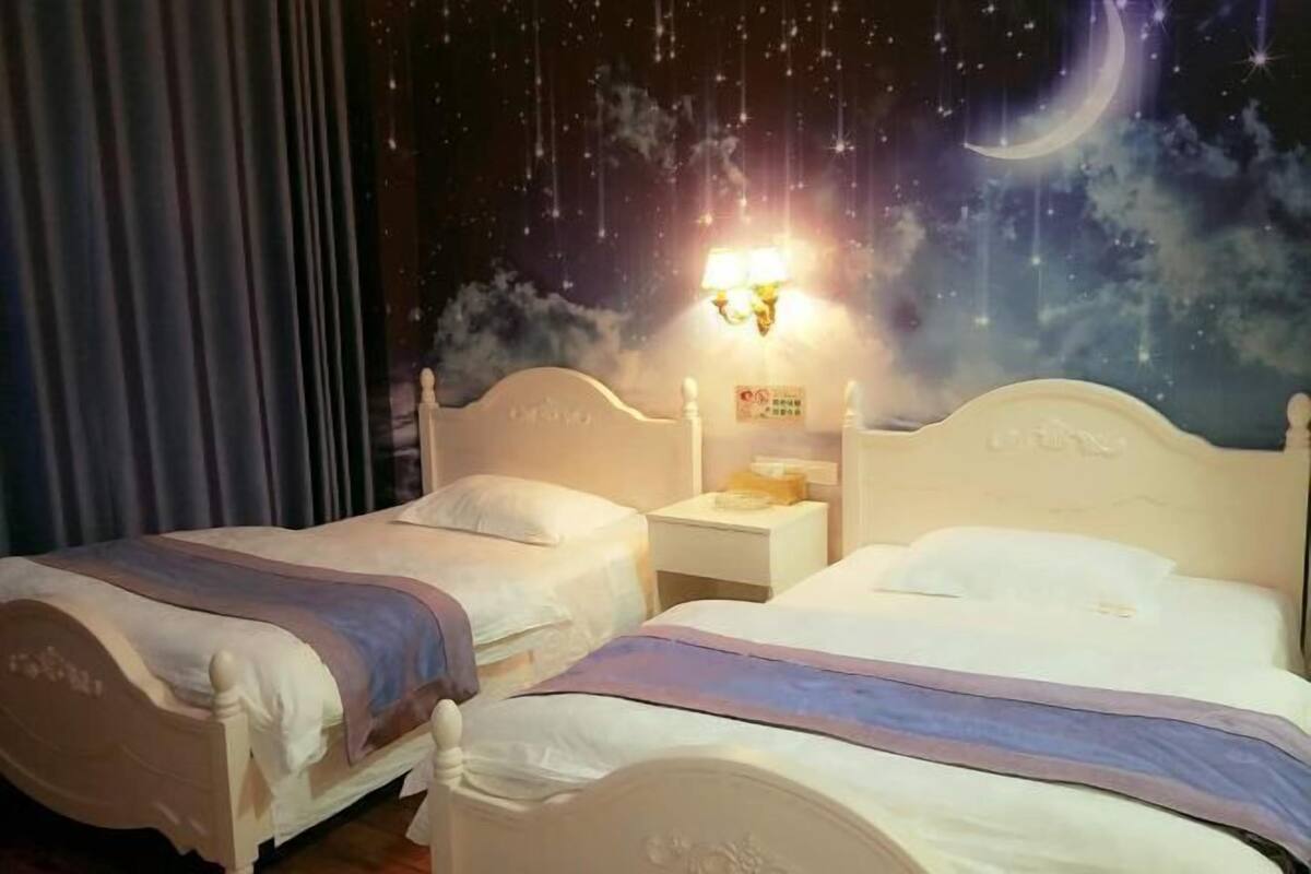A hotel room with two beds, a nightstand, and a wall mural of a starry night sky.