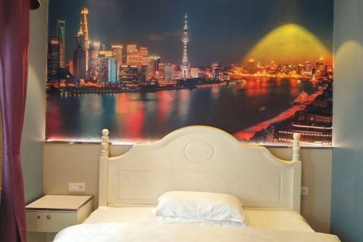 A hotel room with a bed, a nightstand, and a cityscape poster on the wall.