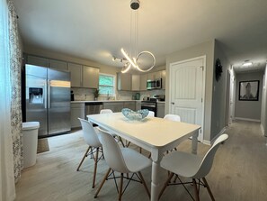 A modern kitchen with stainless steel appliances, a white dining table with chairs, and a pendant light. - Elegant Urban Oasis (Durham)