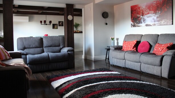 Sala de estar com dois sofás cinza, um tapete listrado em preto e branco e um quadro grande com cores vermelho e branco na parede.