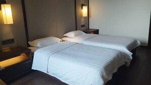 Quarto de hotel com duas camas, mesas de cabeceira, luminárias fixadas na parede e um chão de madeira escura.