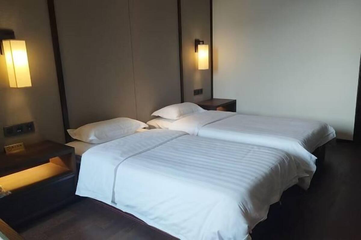 A hotel room with two beds, bedside tables, wall-mounted lamps, and a dark wooden floor.