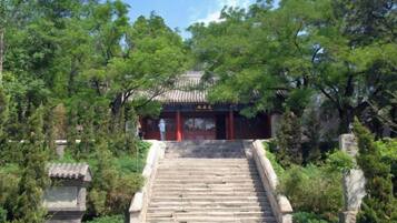 A traditional building with a red entrance, surrounded by trees and a stone staircase leading up to it.