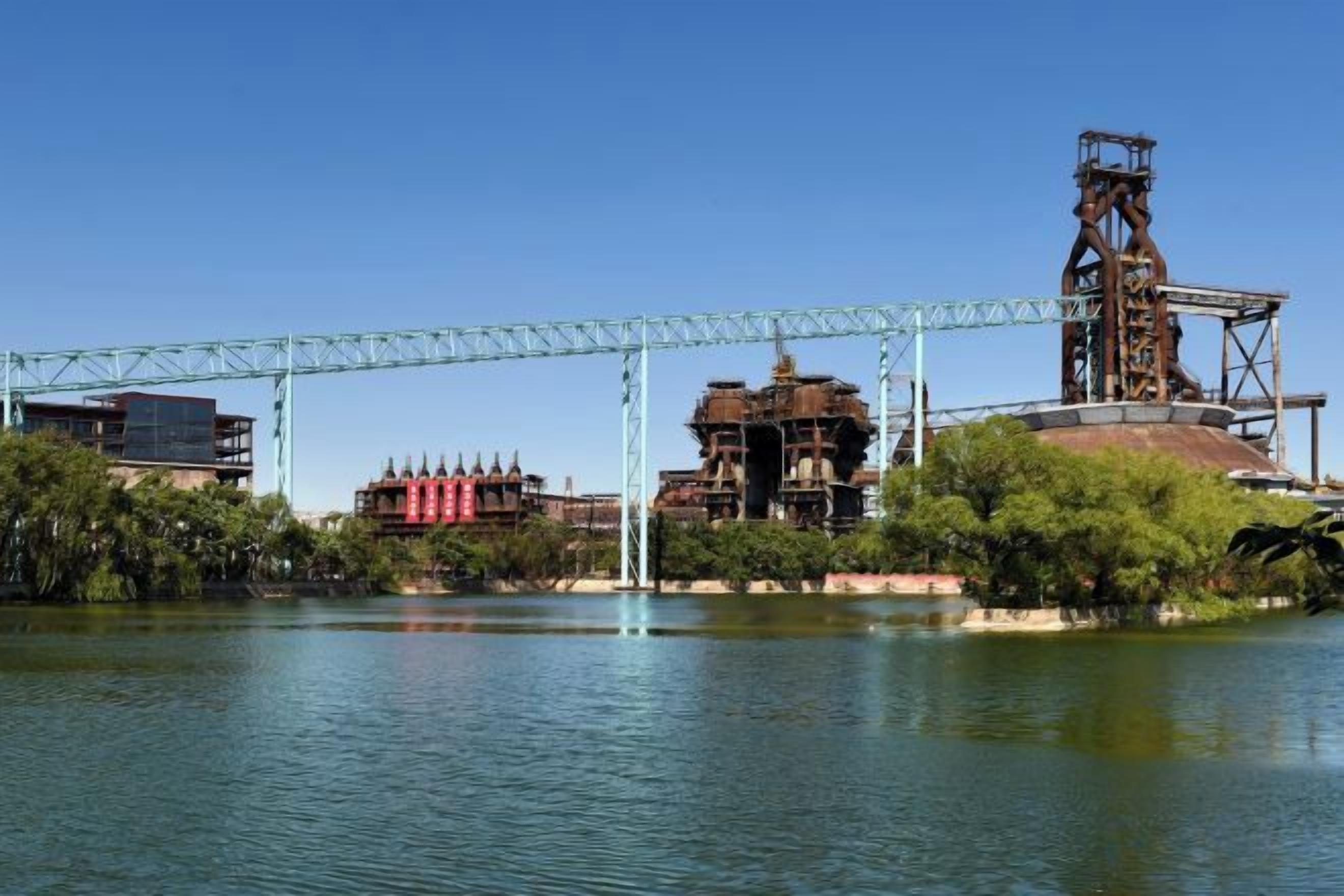Un fiume con un ponte, strutture industriali e un grande edificio con facciata rossa.