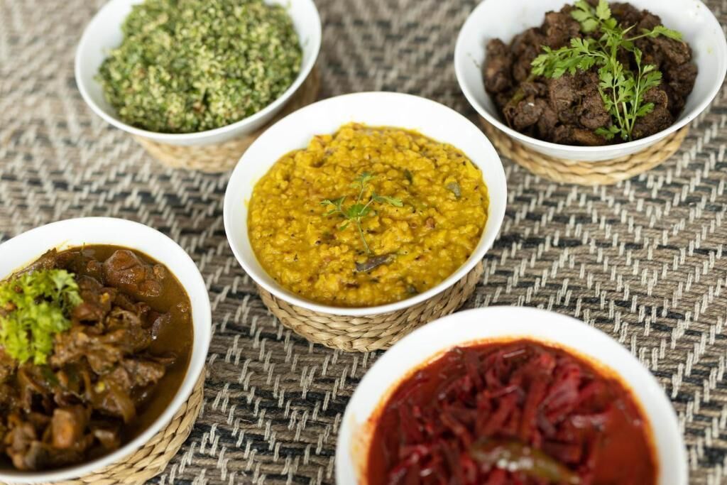 Five bowls of different dishes on a woven mat.