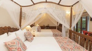 Uma cama com dossel e cortinas, roupa de cama branca, almofadas estampadas, cabeceira de madeira e vista para uma varanda.