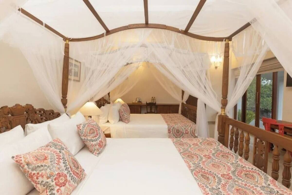 Ein Himmelsbett mit weißer Bettwäsche, gemusterten Kissen, einem Holz-Kopfteil und Blick auf einen Balkon.