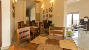 Uma sala de jantar com mobiliário de madeira e jogos americanos trançados, geladeira e luminárias fixadas na parede.