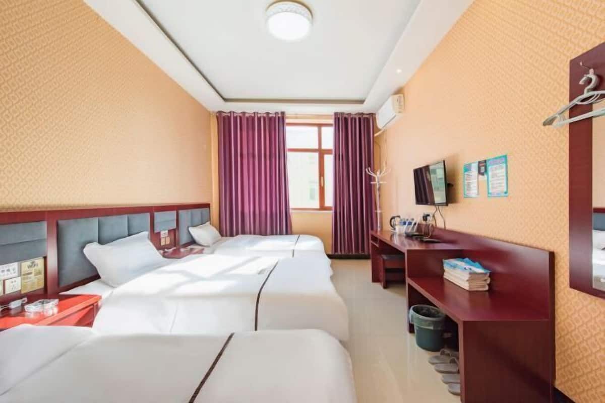 Quarto de hotel com três camas, uma escrivaninha, televisão e janela com cortinas.