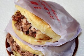 A sandwich with visible fillings, wrapped in paper with text. - jujia lianhe jiudian (Boye)