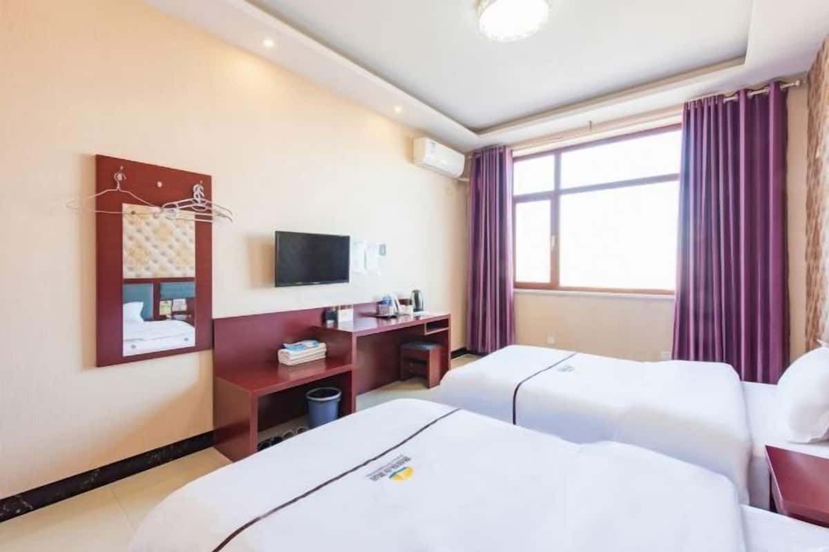 Quarto de hotel com duas camas, uma escrivaninha, televisão e janela com cortinas.