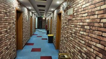 A hallway with brick walls, wooden doors, and a blue carpet with red squares.