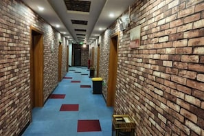 A hallway with brick walls, wooden doors, and a blue carpet with red squares. - jujia lianhe jiudian (Boye)