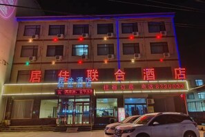 A hotel with a prominent red sign, multiple windows, and a car parked in front. - jujia lianhe jiudian (Boye)