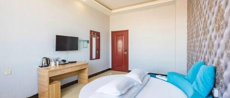 A hotel room with a bed, a desk, a television, and a door.