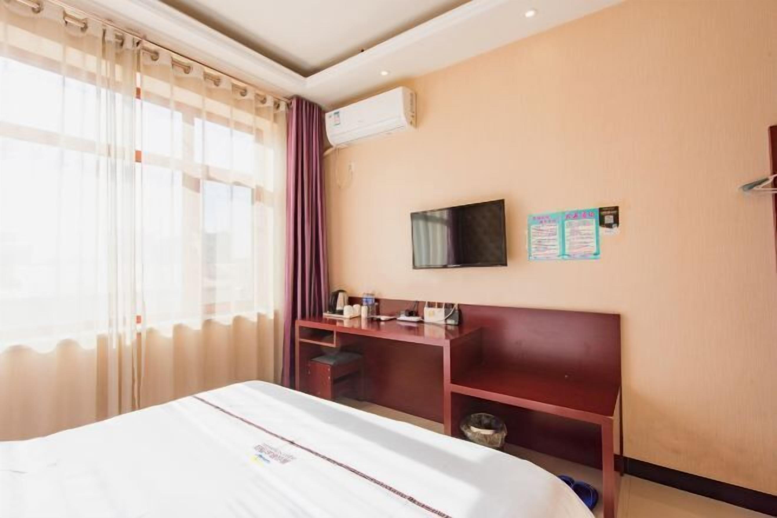 A hotel room with a bed, a desk, a television, and a bulletin board.