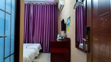 Habitación de hotel con dos camas, cortinas moradas, un escritorio pequeño con espejo y aire acondicionado de pared.