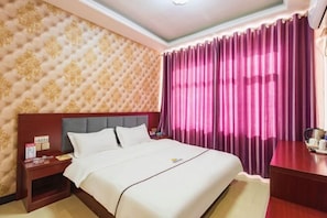 A hotel room with a bed, a nightstand, a wooden desk, and a window with purple curtains. - jujia lianhe jiudian (Boye)