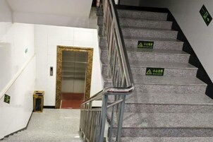 A staircase with handrails and caution signs, leading to an elevator.