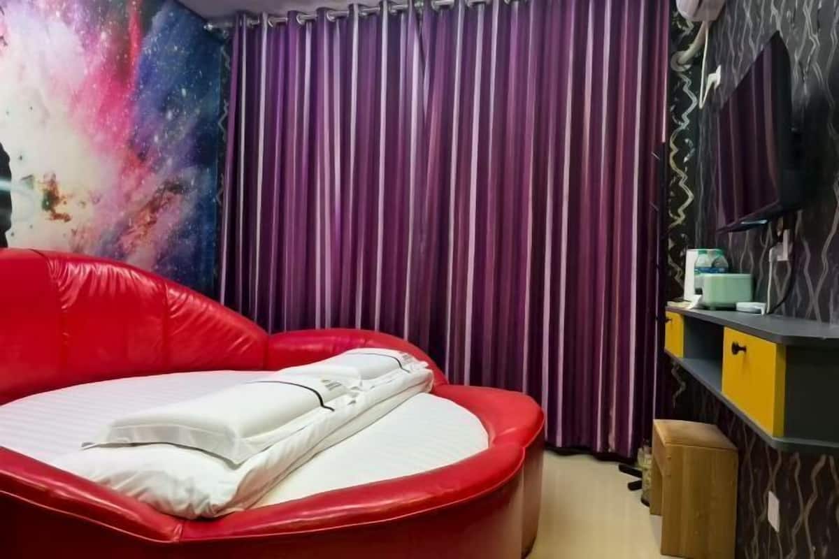 Quarto com sofá-cama vermelho, cortinas roxas, parede com tema de galáxia e um banquinho de madeira.