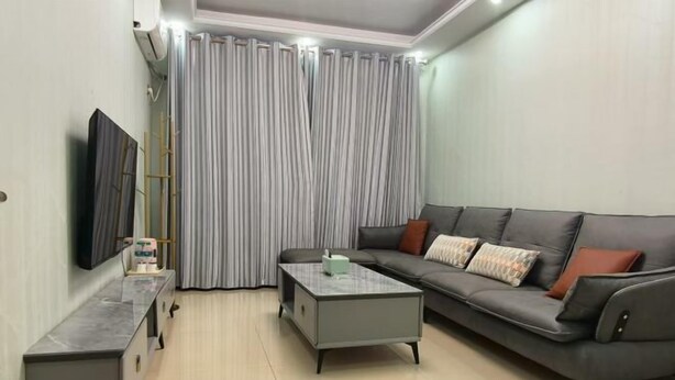 A modern living room with a grey sofa, a coffee table, and a TV on a stand. - jujia lianhe jiudian (Boye)