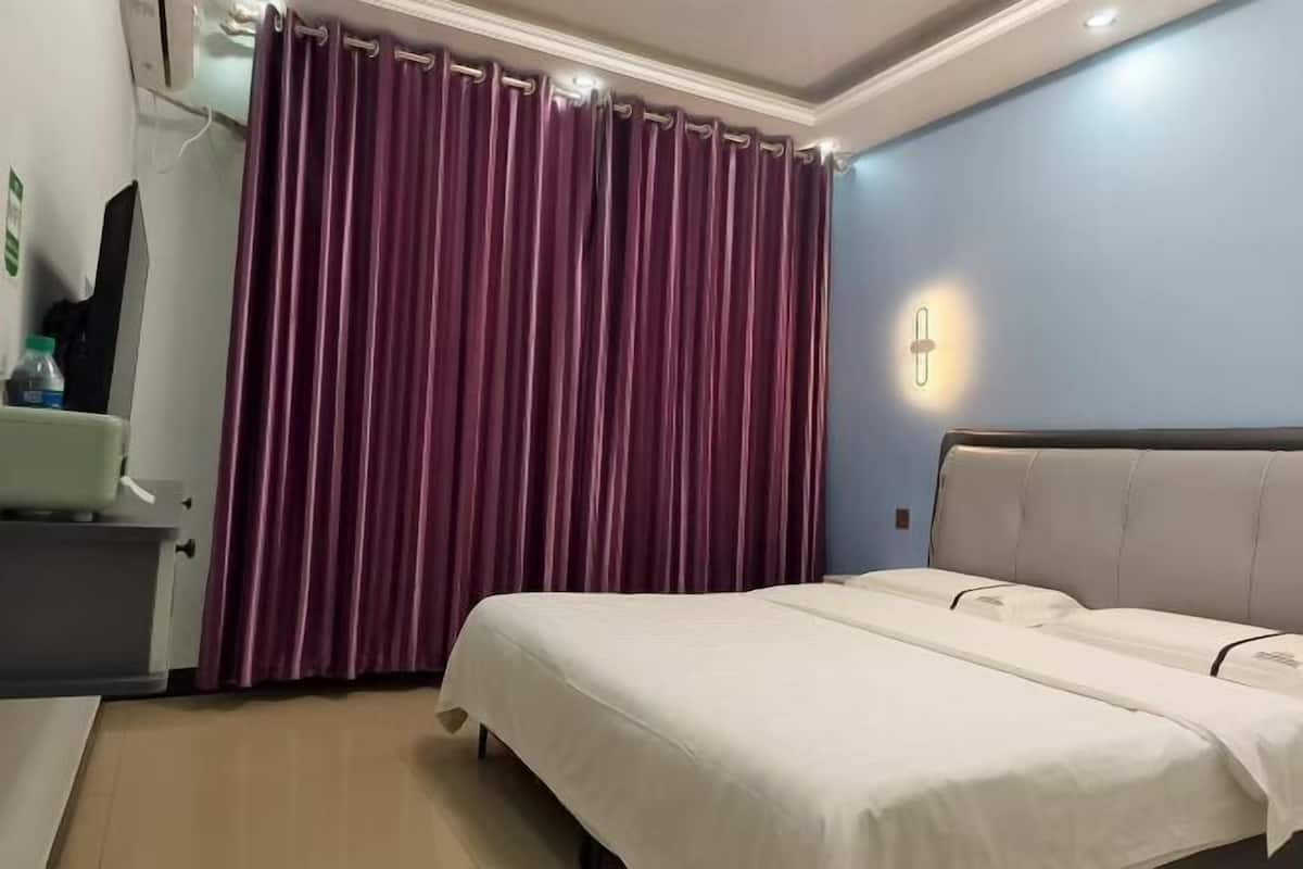 Quarto de hotel com uma cama, mesa de cabeceira, espelho e janela com cortinas roxas.