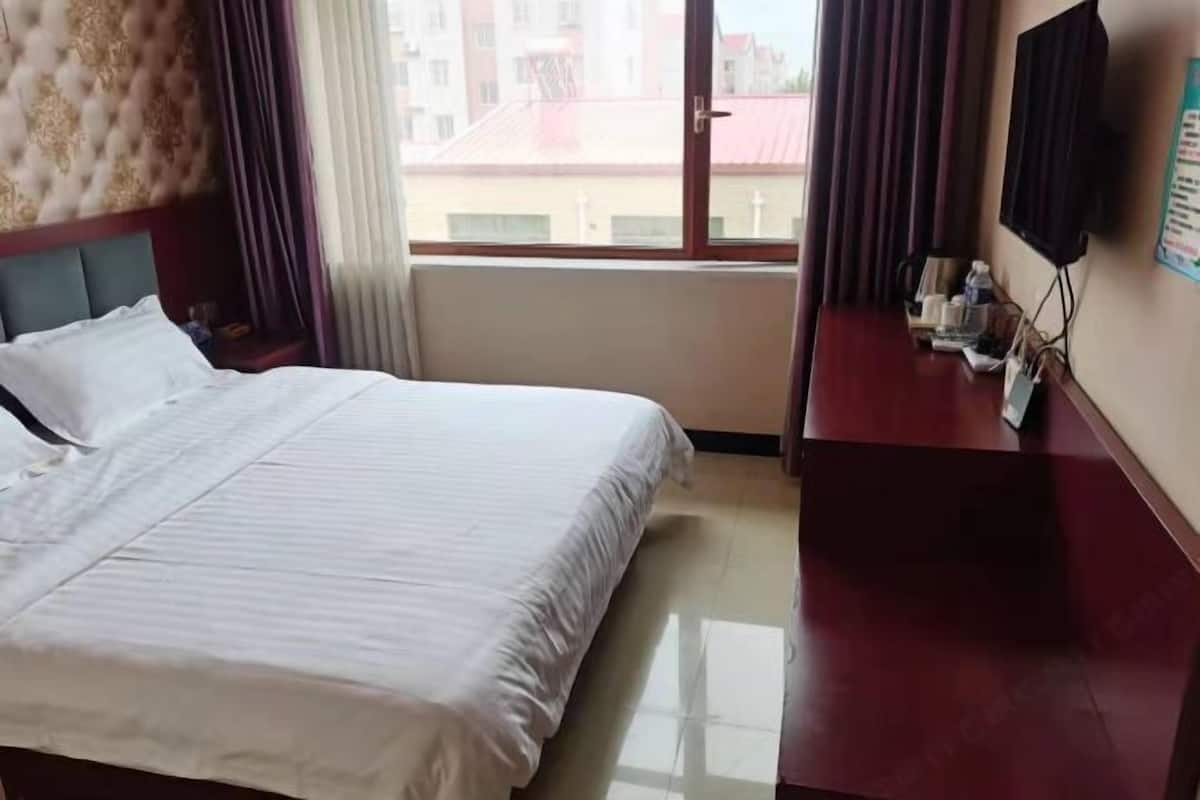 Quarto de hotel com cama, escrivaninha, televisão e janela com cortinas.