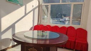 A round glass-top table with a dark wooden base, surrounded by red chairs, in a room with a large window and a view of a bridge. - Xinglong Xiaoshan Farmhouse (Xinglong)