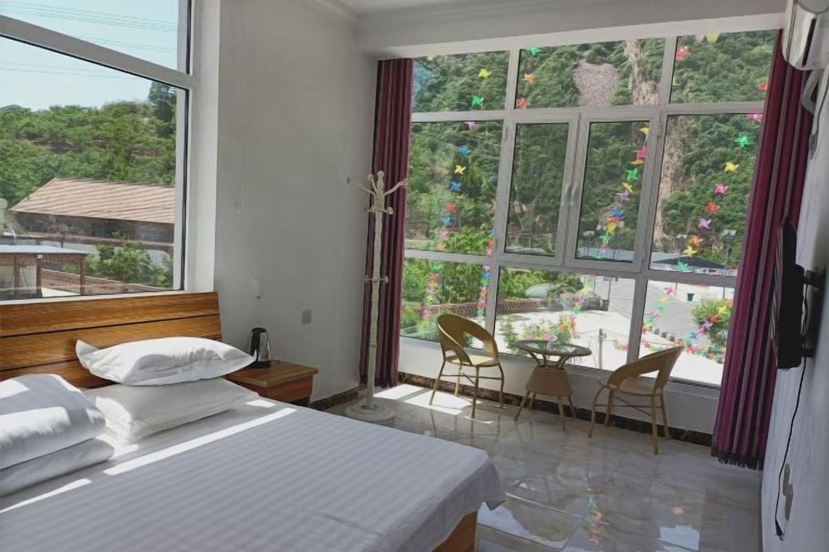A hotel room with a bed, a small table, two chairs, and a window with curtains.