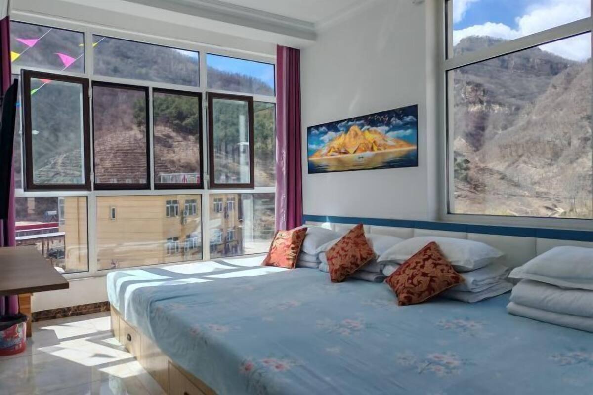 A bedroom with a large bed, multiple windows, and a painting of a mountain landscape.