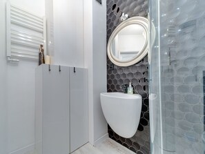 Une salle de bain moderne avec des toilettes blanches, un miroir rond et un mur orné d’un motif circulaire.
