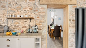 Une cuisine rustique aux murs de pierre, avec des étagères en bois et un coin repas comprenant une table et des chaises en bois.