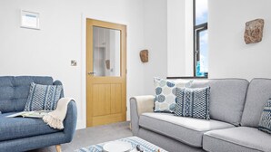 A living room with a blue armchair, a grey sofa, and a coffee table with cheese, tomatoes, and plates. - One of 3 cottages, this beautiful barn conversion with a hot tub and EV charger is the perfect place (Paignton)