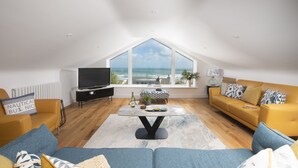 Ein modernes Wohnzimmer mit großem Fenster und Meerblick, einem Flachbildfernseher und einer gemütlichen Sitzecke.