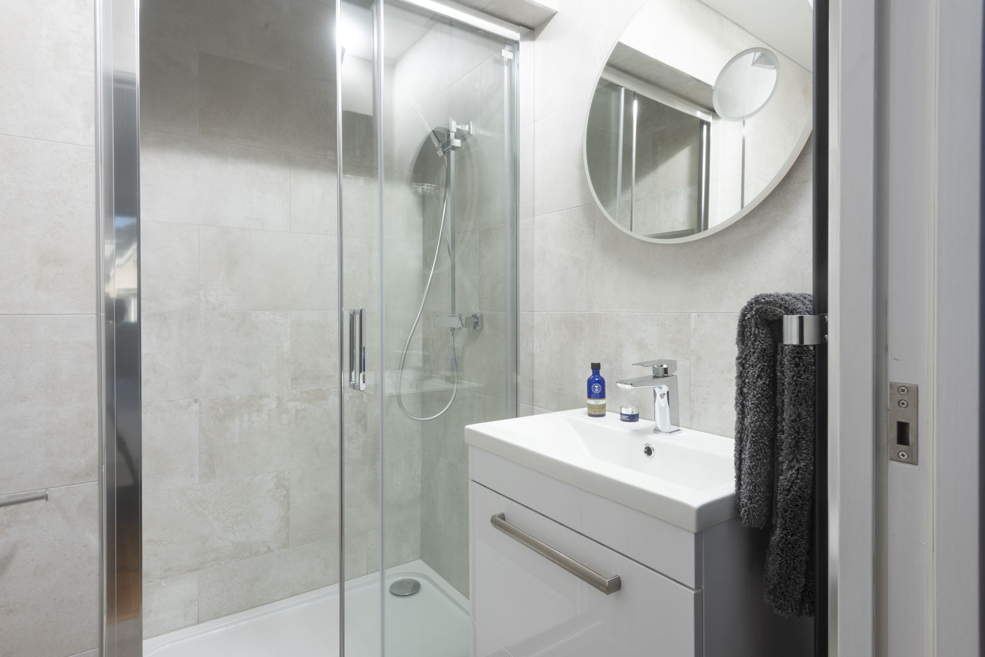 A modern bathroom with a glass-enclosed shower, a white sink, and a round mirror.