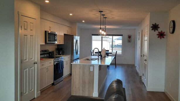 A modern kitchen with white cabinets, stainless steel appliances, and a central island. - Home in Fort Saskatchewan (Fort Saskatchewan)