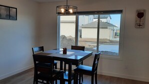 A dining area with a table and chairs, a pendant light, and a view of a construction site through a large window. - Home in Fort Saskatchewan (Fort Saskatchewan)