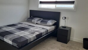 A modern bedroom with a bed, bedside tables, and a window. - Home in Fort Saskatchewan (Fort Saskatchewan)