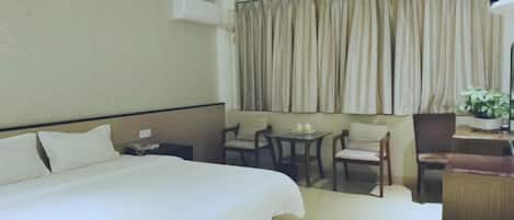 Habitación de hotel con una cama grande, un escritorio, dos sillas, una mesita y una planta en maceta.