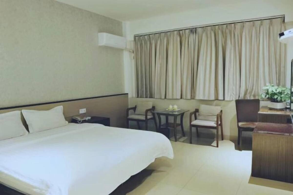 Une chambre d’hôtel avec un grand lit, une petite table avec des chaises, un bureau avec une chaise et une fenêtre avec des rideaux.