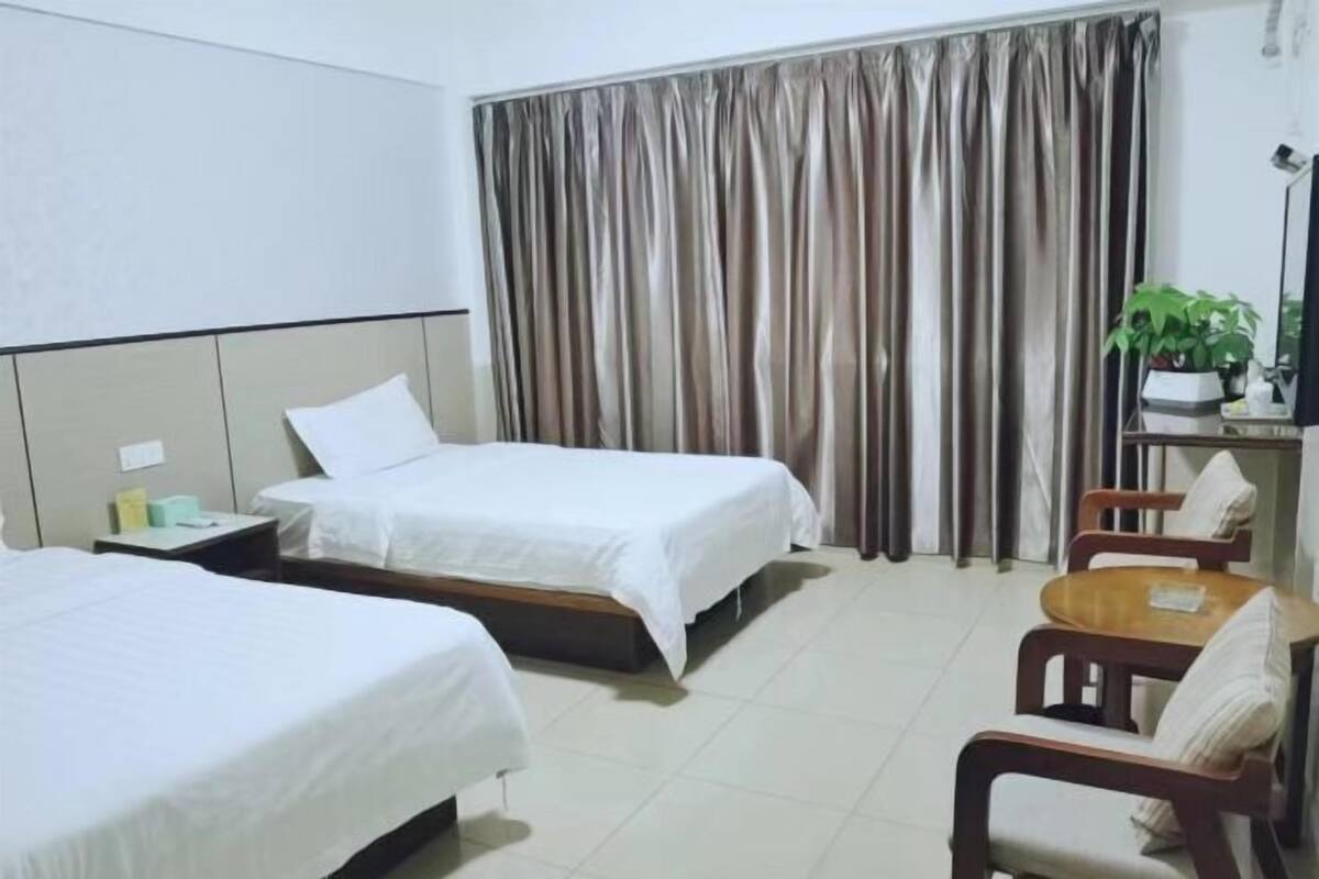 Une chambre d’hôtel avec deux lits, une petite table, une chaise, un bureau avec une lampe et un rideau.