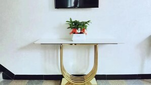 Een moderne kamer met een witte tafel, een potplant en een flatscreen televisie aan de muur.