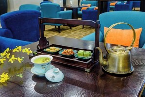 Un juego de té con tetera y tazas sobre una mesa de madera, acompañado de una bandeja con diversos alimentos.