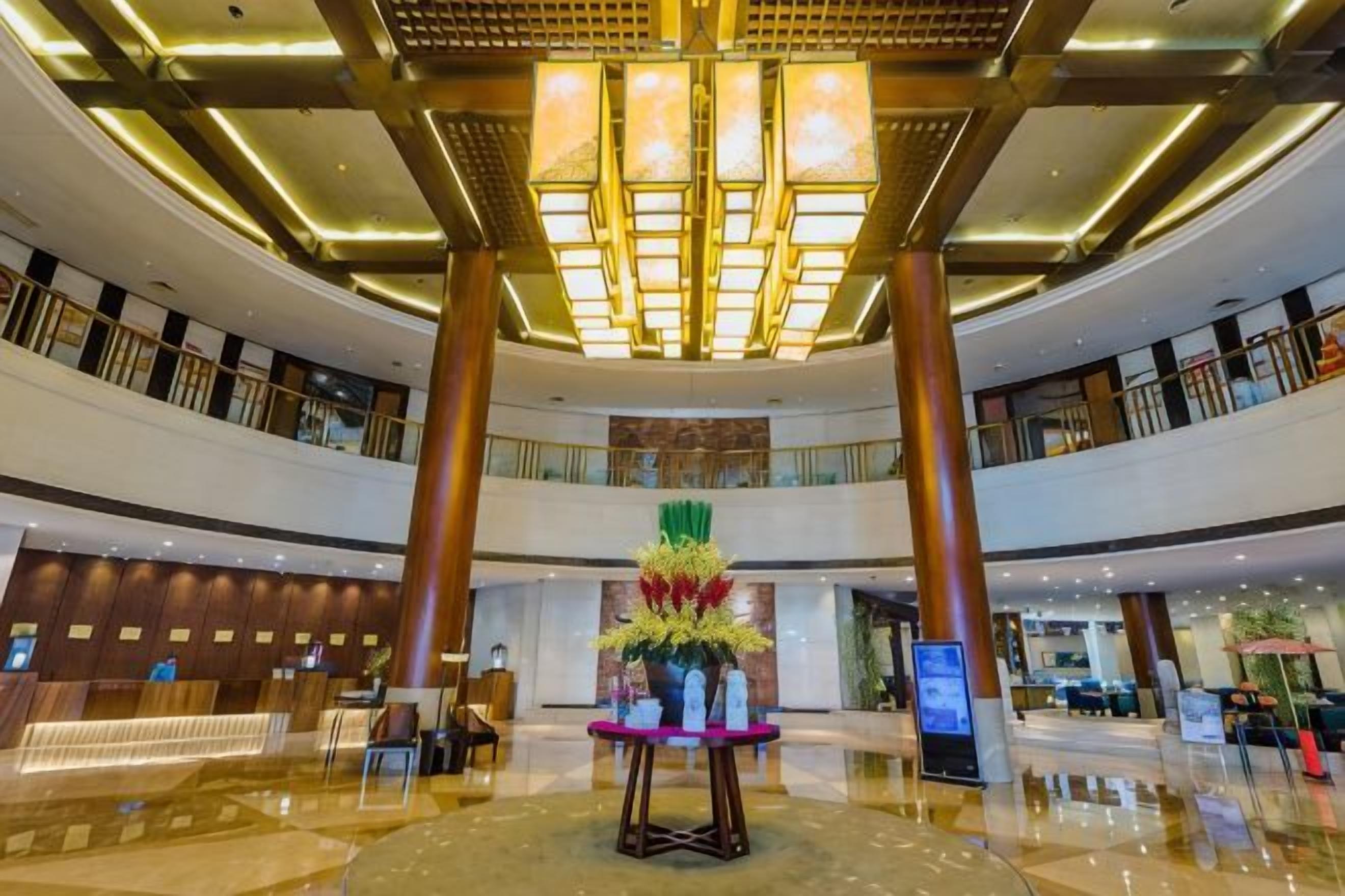 A spacious lobby with a central reception desk, high ceilings, and a modern chandelier.