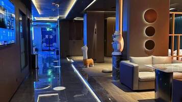 A modern hotel lobby with a long corridor, a reception desk, and a seating area with a sofa and a table.