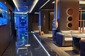 A modern hotel lobby with a long corridor, a reception desk, and a seating area with a sofa and a table.