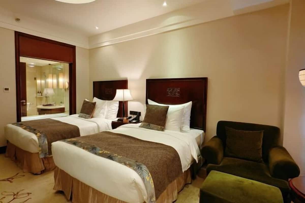 Een hotelkamer met twee bedden, een stoel, een nachtkastje en een spiegel.