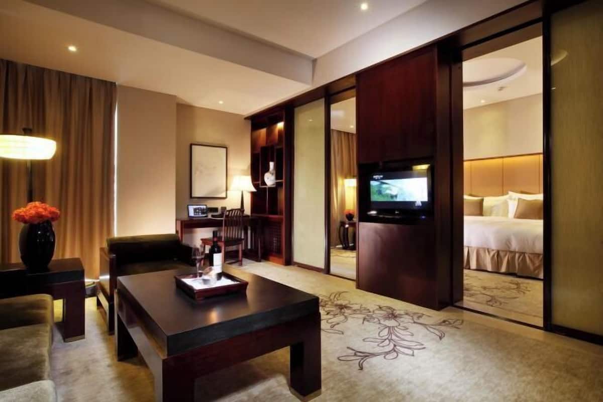 Een hotelkamer met een bank, een salontafel, een televisie, een bed en een schuifdeur naar een andere kamer.