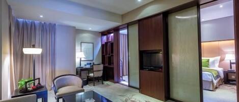 Habitación de hotel con sofá, mesa de centro, televisor, escritorio y cama.