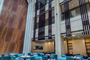 Een hotel lobby met een hoge plafond, marmeren wanden en een zithoek met blauwe stoelen en tafels.